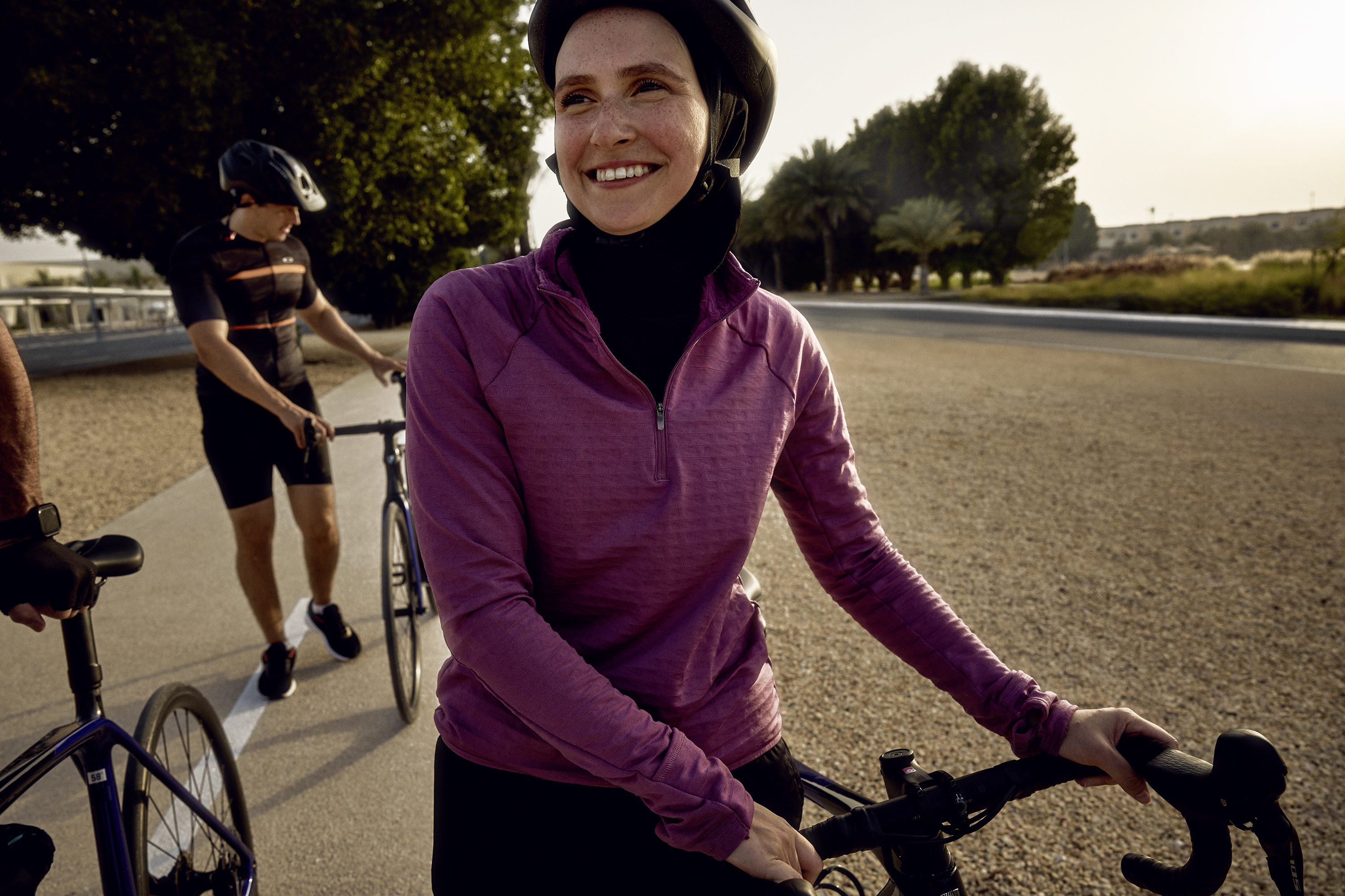 A woman in a helmet and hijab holds her bicycle on a cycle path, while another rider walks a bike behind her.
